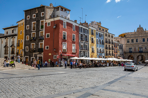 Plaza Mayor with colorful houses, crowded restaurant terraces. It is a sunny day in Spring with people sit under parasols.