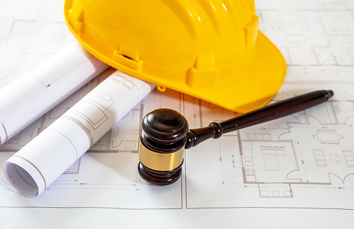 Labor, Construction law. Yellow safety hardhat and judge gavel on building blueprint plans