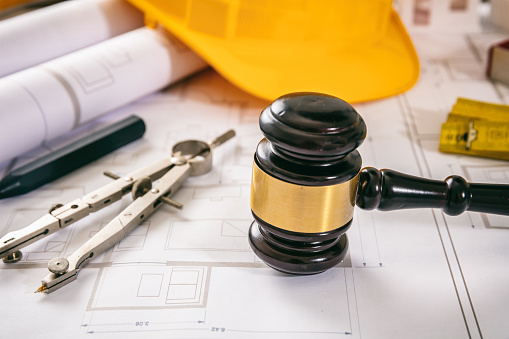 Construction and Labor law. Yellow safety helmet and judge gavel on building blueprint plans, close up view.