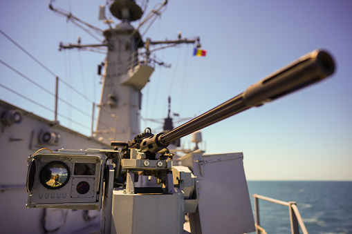 Color image of an automated machine gun on the deck of a military ship, at sea.