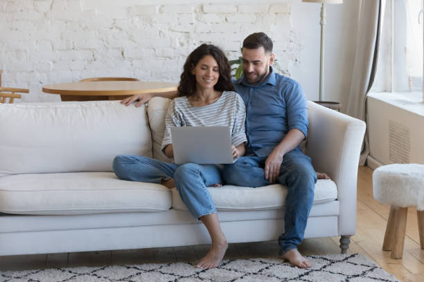 Happy engaged millennial couple in love sitting on couch stock photo