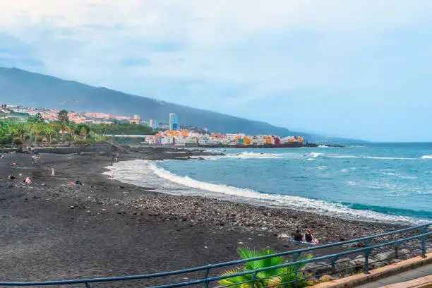 Playa del Castillo beach on the Atlantic coast in Puerto de la Cruz, Spain. Few people on a black sand beach during a storm in the Canary Islands