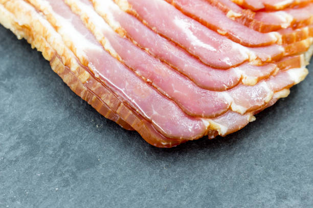 istock Slices of quality bacon on a black slate board. Closeup. 1414801748