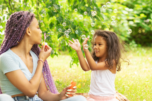 modern young mother and daughter spend time together, parent with happy child play in nature with soap bubbles on a sunny summer day