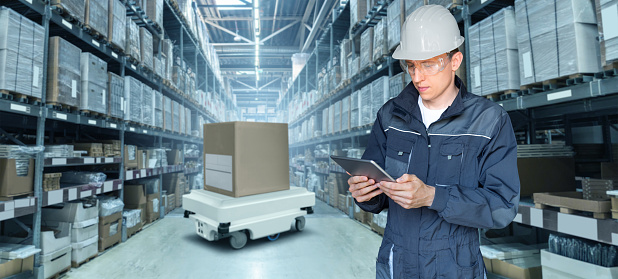 Warehouse manager with digital tablet controls robot with a package. Unmanned delivery concept