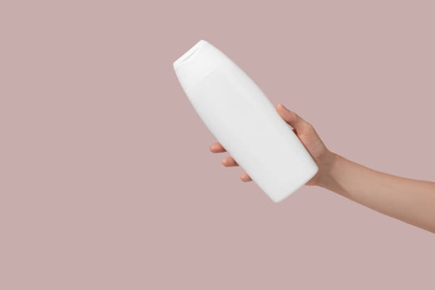 Hand holding blank white plastic tube on pink background. Cosmetic beauty product branding mockup. Copy space stock photo