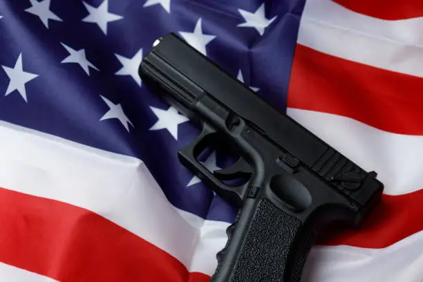 A black pistol lies against the background of the American flag. Personal weapons of the population. Close-up. Permission to carry weapons. Self-defense. The concept of protecting personal property and life