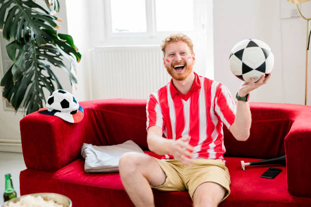 istock Ginger man cheering while watching tv at home 1414814744