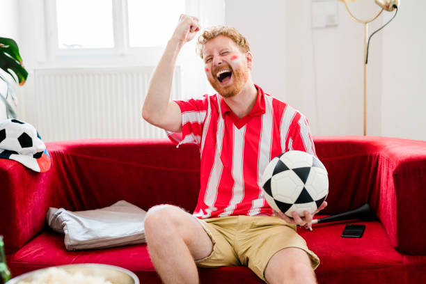 istock Ginger man cheering while watching tv at home 1414814757
