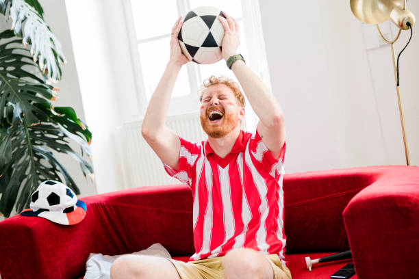 istock Ginger man cheering while watching tv at home 1414814823