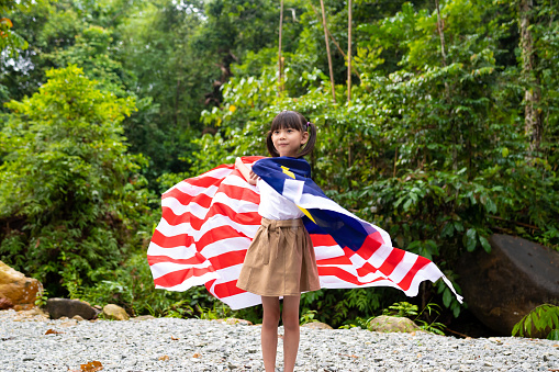 Young Asian girl waving Malaysian flag with pride. High Independence Day Spirit and Patriotism, Malaysia National Day Concepts.