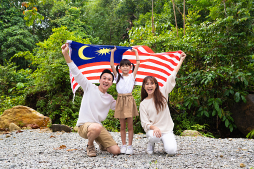 Young Asian family waving Malaysian flag with pride. High Independence Day Spirit and Patriotism, Malaysia National Day Concepts.