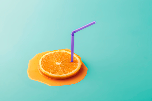 Creative summer concept with copy space. A sliced orange slice with a straw and a rasping juice on a blue background.