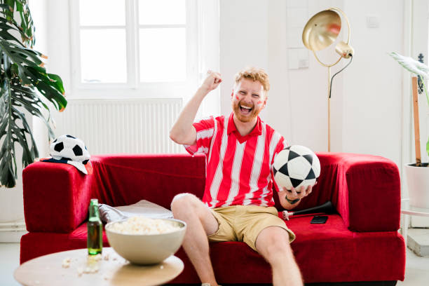 istock Ginger man cheering while watching tv at home 1414820817
