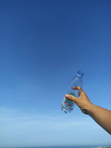 istock Transparent mineral water bottle in hand on bright blue sky background. 1414823132