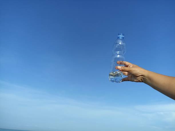 istock Transparent mineral water bottle in hand on bright blue sky background. 1414823251