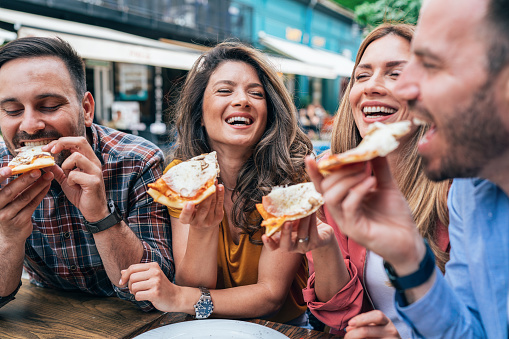 Group of happy young friends eating pizza together, outdoor. Cheerful friends eating pizza, smiling and talking, enjoying the day and have fun. Fast food
