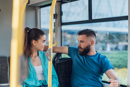 Young couple of friends chatting on a bus together. Two best friends are talking while sitting in a bus. People in a public transport concept. Modern city vehicle. Romantic couple in city transport.