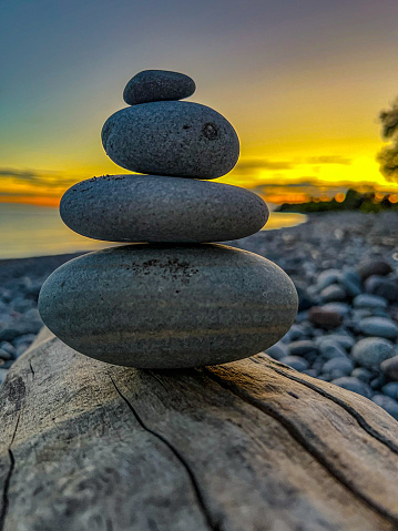 Stack of stones on a piece of driftwood on the shore as the sun sets