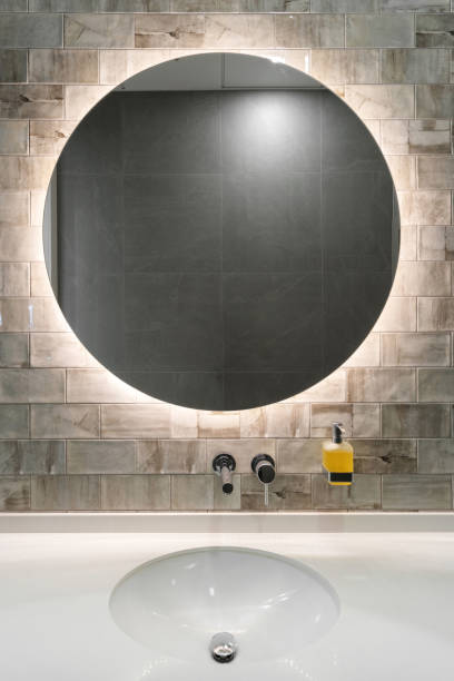 white washbasin, water faucet and round mirror on wall in bathroom modern bathroom interior with stone tile on wall, ceramic white washbowl, water tap, dispenser with liquid soap and illuminated mirror indoors restaurant mirror stock pictures, royalty-free photos & images