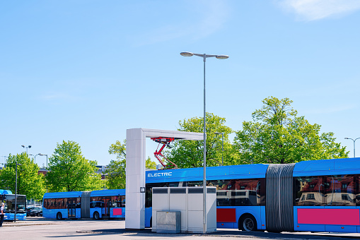 City station for recharging electric public transport. Several urban shuttle buses are connected to electric charging equipment against the background of the urban landscape