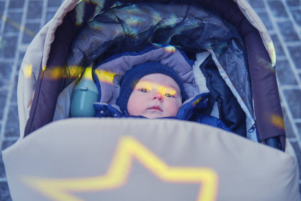Baby infant boy in a hat and winter clothes is lying in a stroller. A child aged six months on an outdoor walk Baby infant boy in a hat and winter clothes is lying in a stroller. A child aged six months on an outdoor walk baby stroller winter stock pictures, royalty-free photos & images