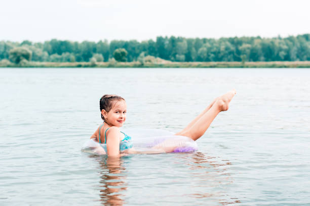 ein fröhliches mädchen schwimmt auf einem aufblasbaren ring im fluss und streckt ihre beine aus. lokaler tourismus. sommerferien - swim ring stock-fotos und bilder