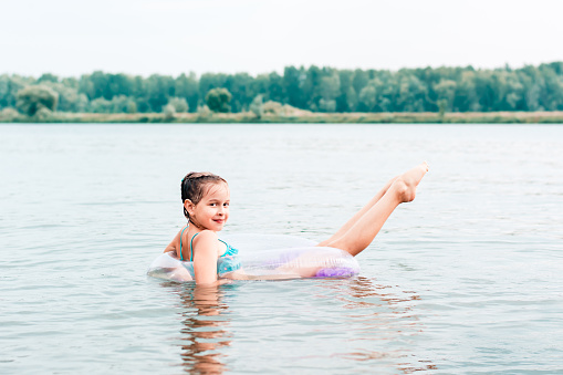 A cheerful girl swims on an inflatable ring in the river and stretches her legs. Local tourism. Summer vacation