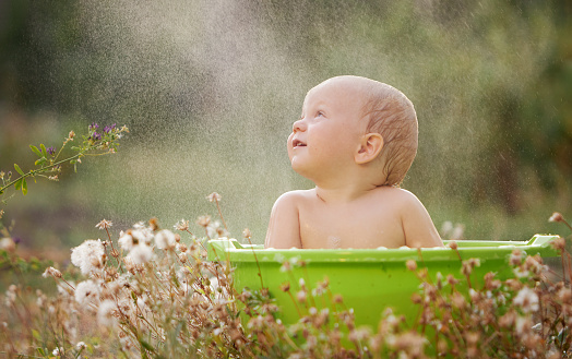 A small child plays in a bowl of water in a summer garden on a sunny day