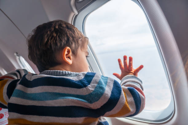 Boy traveling by plane on vacation looking out the window, watching take off stock photo