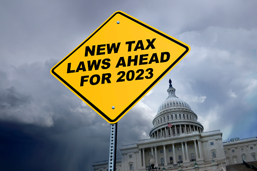 A road sign warning about new tax laws enacted or proposed for 2023 in front of the U.S. Capitol building with stormy skies in the background.