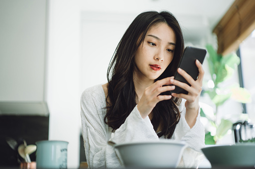 Young Asian woman using smartphone at home. She looks worried.