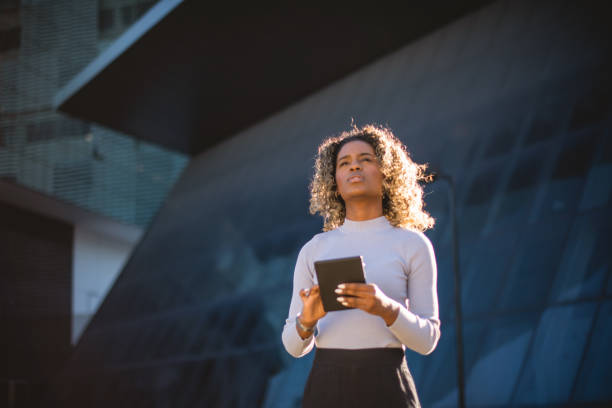 istock woman using tablet in front of a mirrored building 1414863112