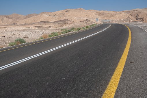 Winding empty road through the south of Israel through the Negev desert. Road curves into the rock desert landscape.