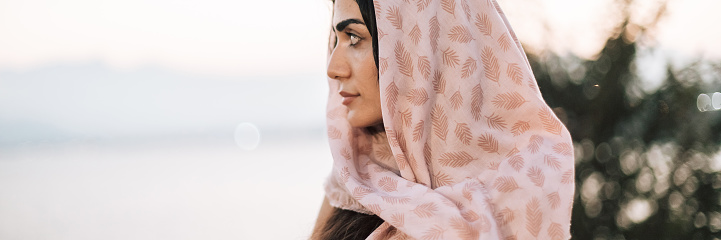 Female portrait of beautiful muslim woman who wear pink headscarf like hijab. Lifestyle photography of nice oriental people. Girl is brunette with dark skin and brown eyes. Person wearing in arabic style