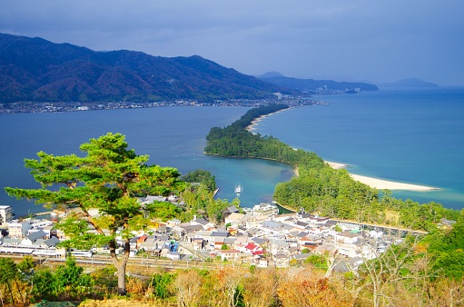 Kyoto, Japan -Desember 7, 2018: Amanohashidate is a sand bar at the mouth of the bay that separates Miyazu Bay in Miyazu City, Kyoto Prefecture from the north and south of the Aso Sea inland sea.Length 3.6km, Width 20-170m.
Amanohashidate, which cuts through the Aso Sea from Miyazu Bay, has long been said to resemble a dragon climbing into the sky.
It is a mysterious form created by nature over thousands of years.It is one of the three scenic spots in Japan.5,000 pine trees grow here, and a white sandy beach spreads out on the east side. Most pine trees are naturally occurring.