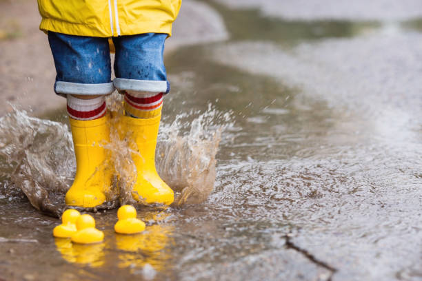 istock A small child in rainbow socks, yellow rubber boots and a jacket runs through puddles, has fun and plays after the rain. A picture of summer and autumn holidays. Legs close-up. 1414871460