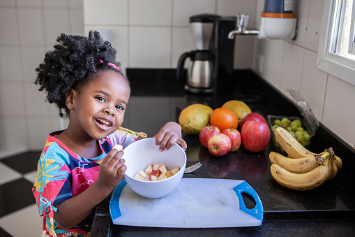 Portrait of little girl eating fruits in the kitchen