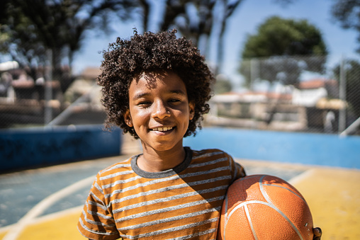 Portrait of a boy holding a basketball ball at a sports court