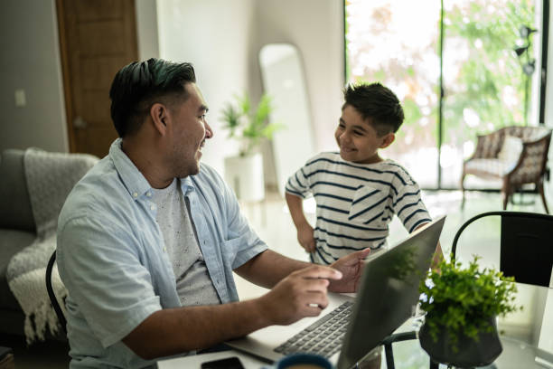 istock Father using laptop working and talking to his son at home 1414877799