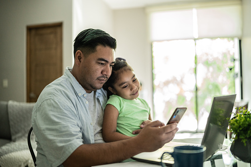 Father working with his daughter using laptop and mobile phone at home