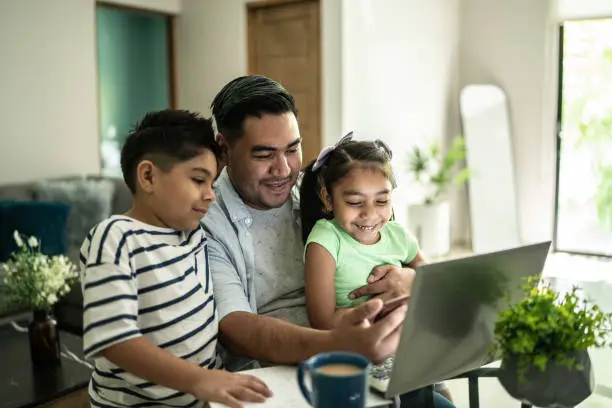 Photo of Father with his kids using laptop and mobile phone watching something at home