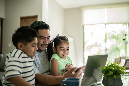 Father with his kids using laptop and mobile phone watching something at home