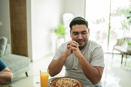 Mid adult man praying before eating lunch at home