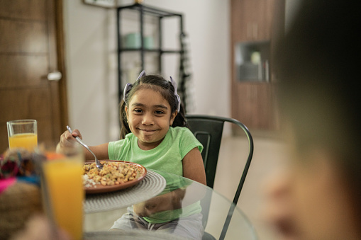 Portrait of little girl eating lunch with her family at home