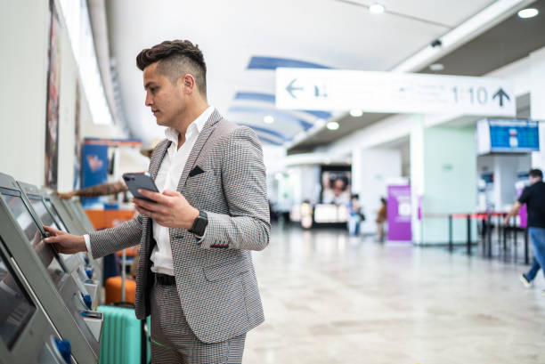 businessman doing check-in and using phone at the airport - self service stockfoto's en -beelden