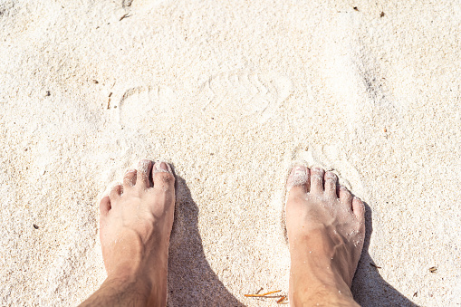 2 feet on the bleach. Close up of young man feet on a tropical sandy beach.