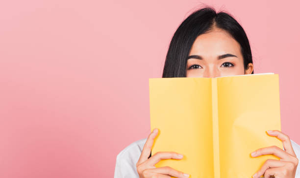 woman teen smile covering her face with yellow book stock photo