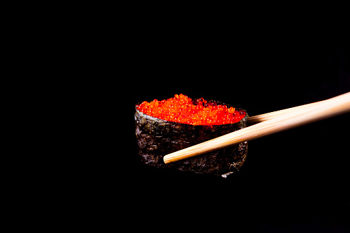 A Tobiko Roe Sushi being held by wooden chopsticks
