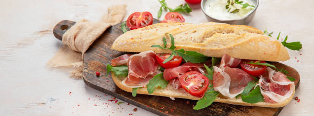 istock Fresh crispy baguette deli sandwich with prosciutto, tomatoes and arugula. 1414898673